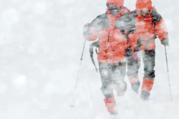 un grupo de alpinistas en una tormenta de nieve y tratando de prevenir una hipotermia con la ropa adecuada que tiene